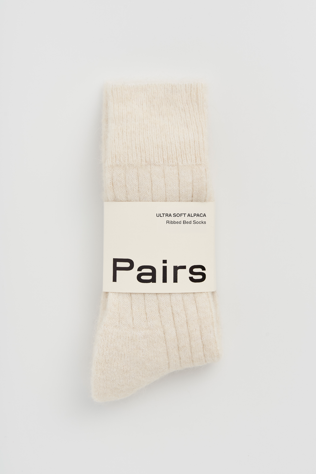 Pair of cream ultra soft alpaca ribbed bed socks with a 'Pairs' packaging band on a light grey background