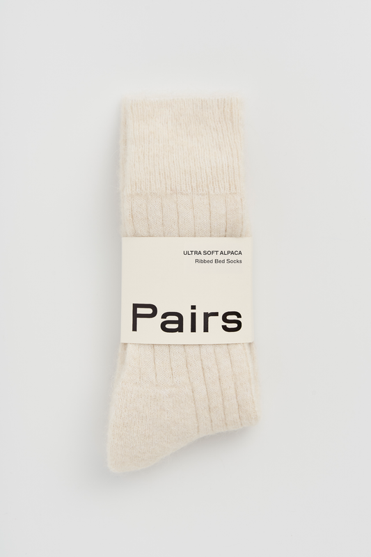 Pair of cream ultra soft alpaca ribbed bed socks with a 'Pairs' packaging band on a light grey background