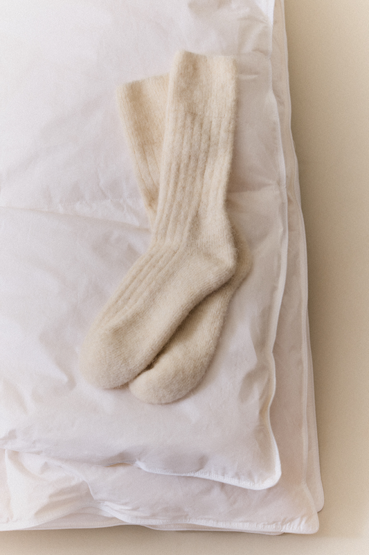 Pair of cream ultra soft ribbed alpaca bed socks on a white pillow with a neutral background