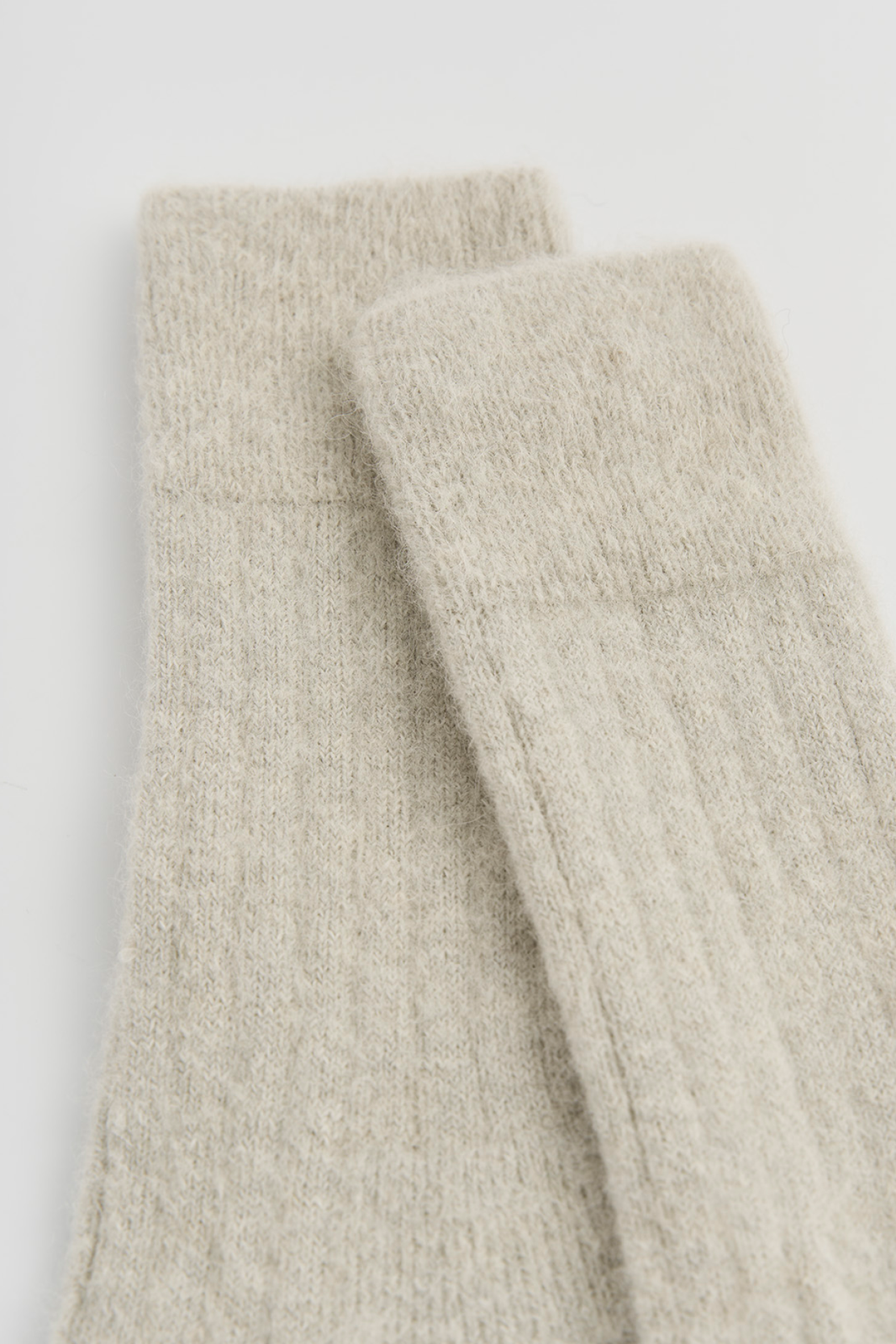 Close-up of the tops of a pair of light grey ribbed ultra soft alpaca bed socks on a light grey background