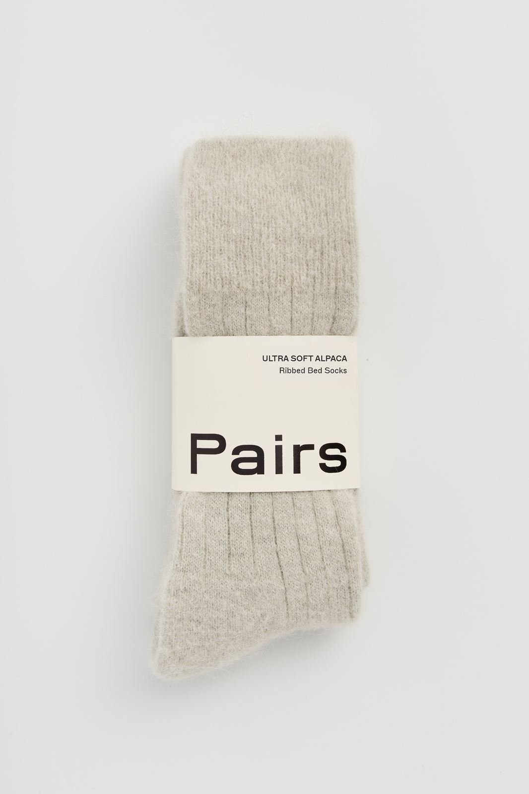 Pair of light grey ribbed ultra soft alpaca bed socks with a 'Pairs' packaging band on a light grey background