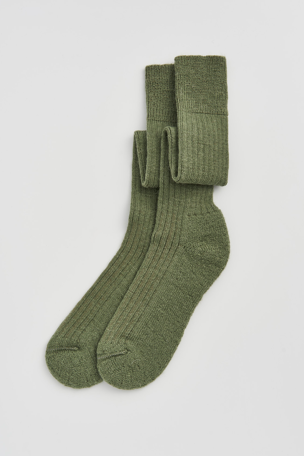 Pair of green wool knee high socks on a light grey background