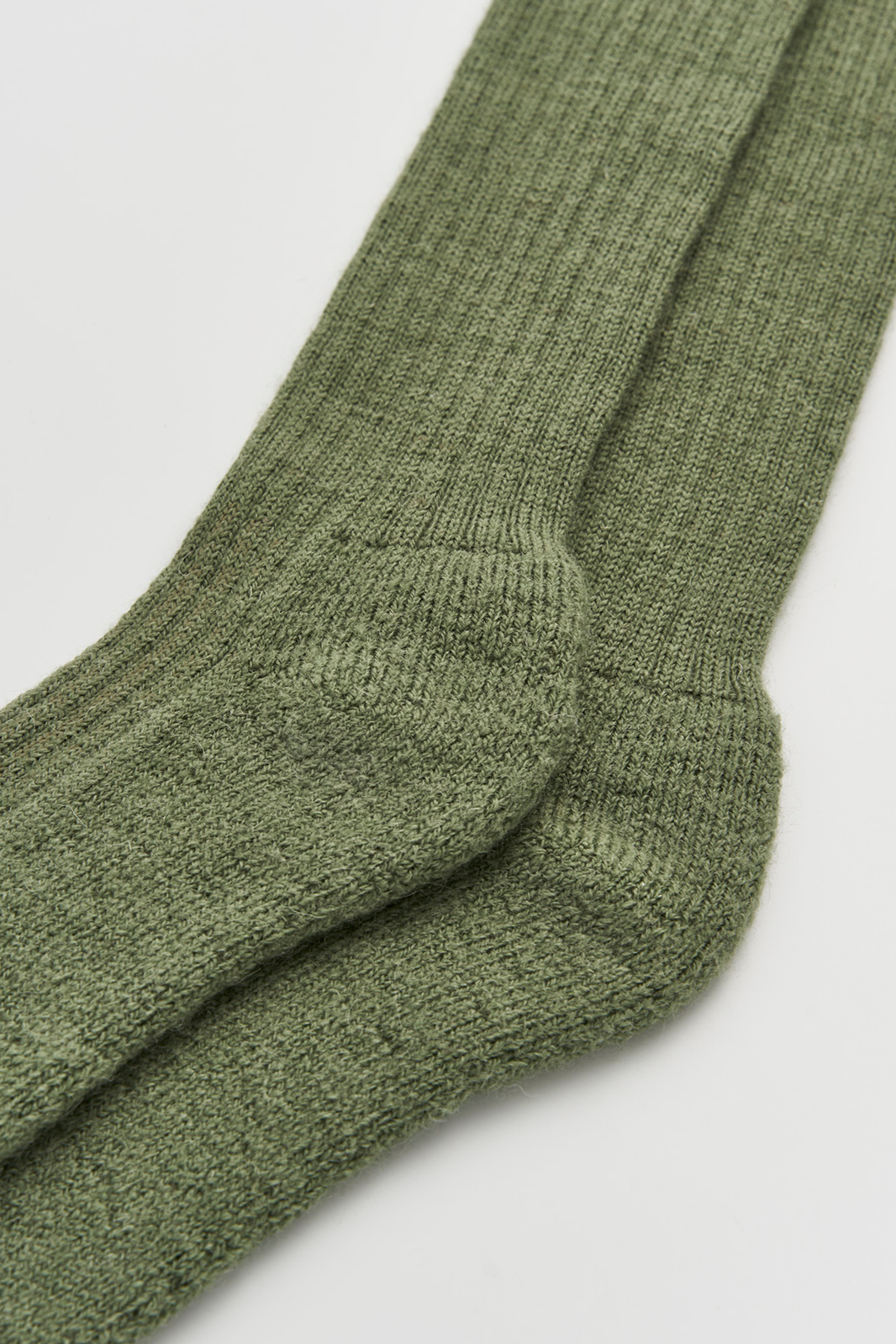 Close-up of the heel of a pair of green wool knee high socks on a light grey background