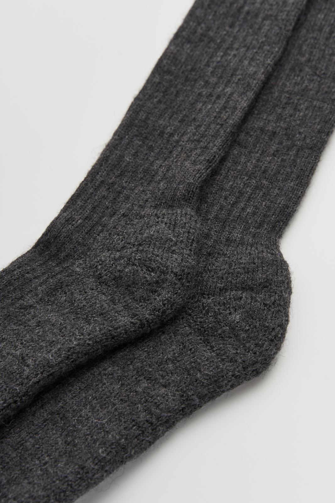 Close-up of the heel of a pair of dark grey wool knee high socks on a light grey background