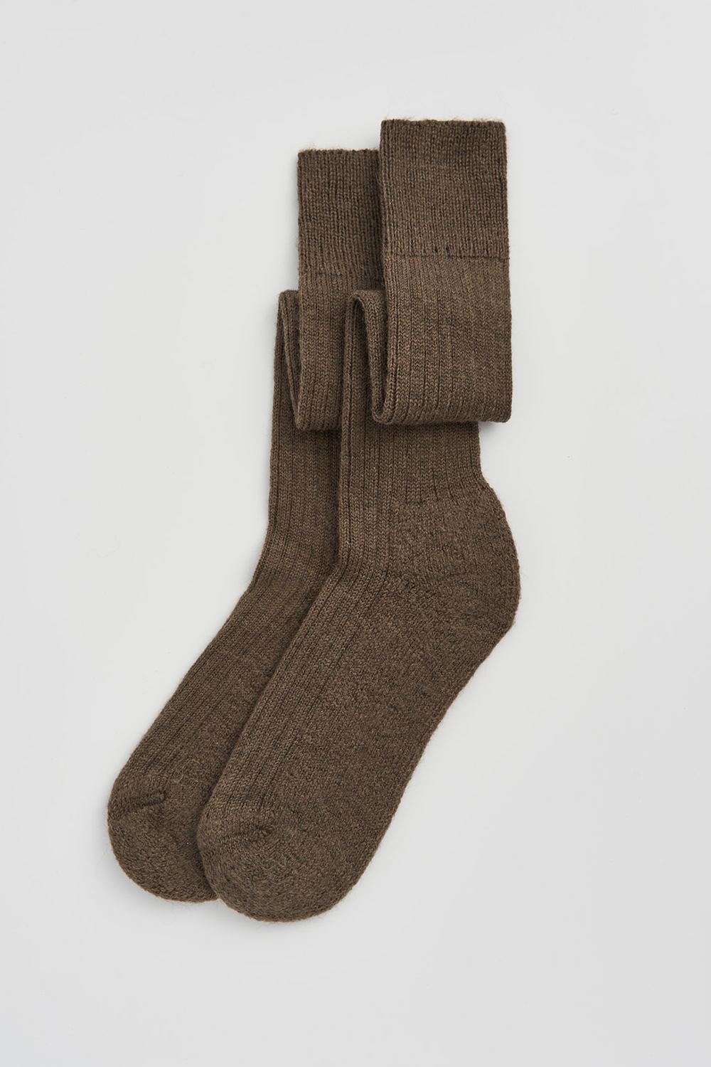 Pair of muddy green wool knee high socks on a light grey background