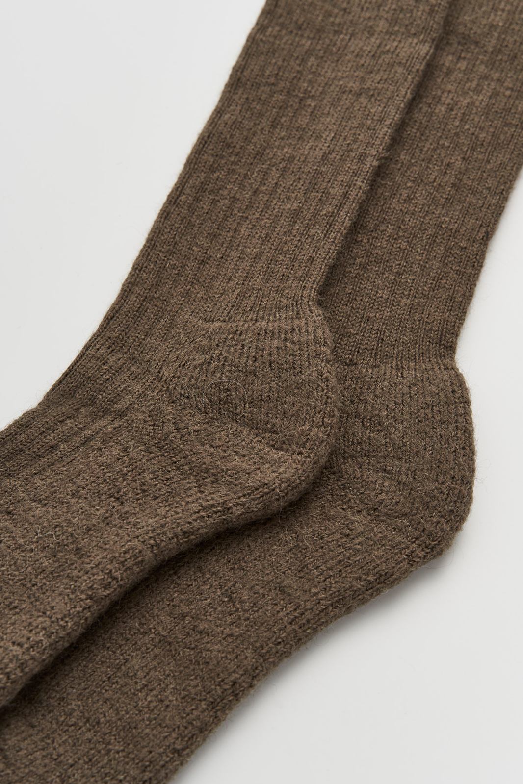 Close-up of the heel of a pair of muddy green wool knee high socks on a light grey background