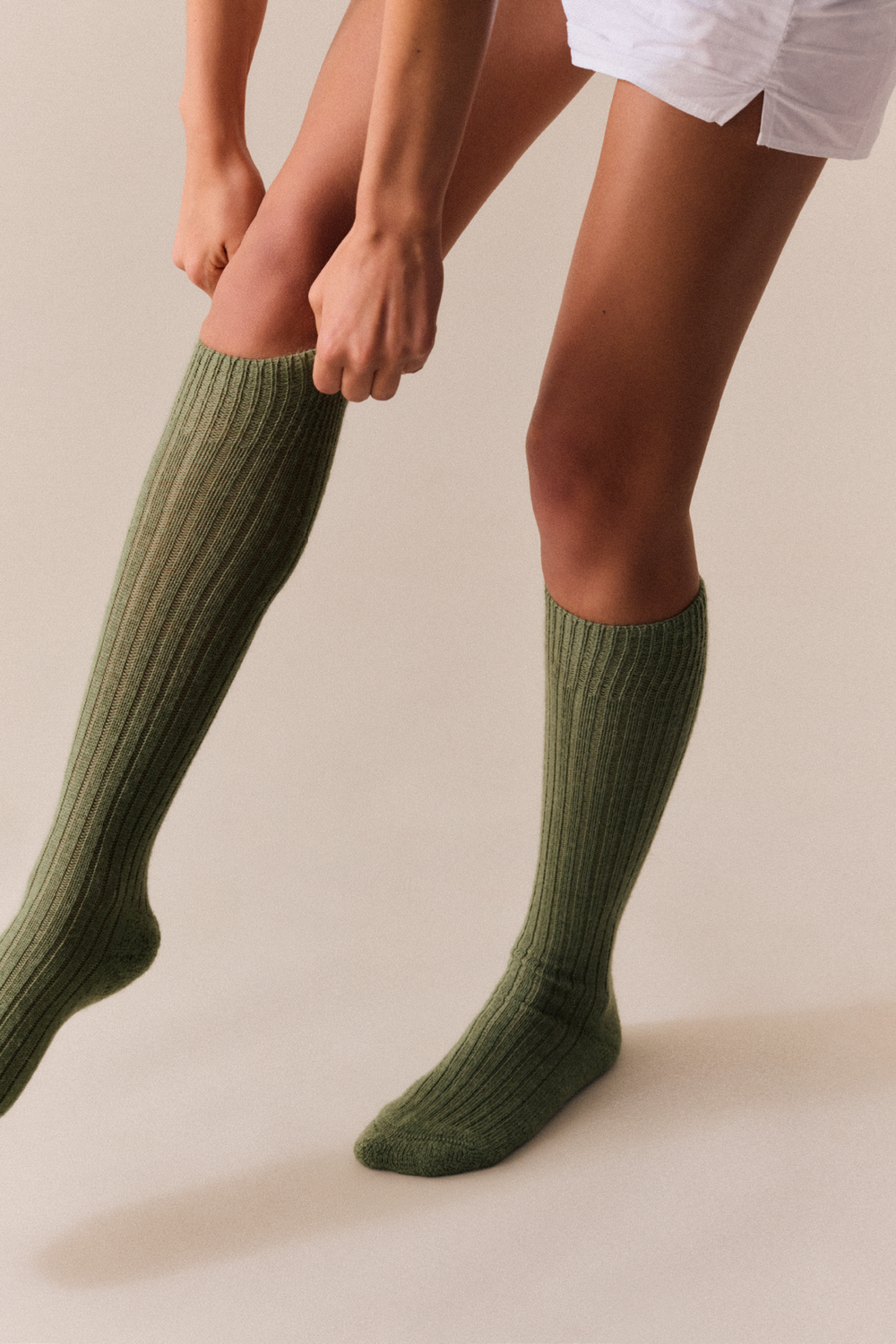Person wearing green wool knee high socks on a plain background