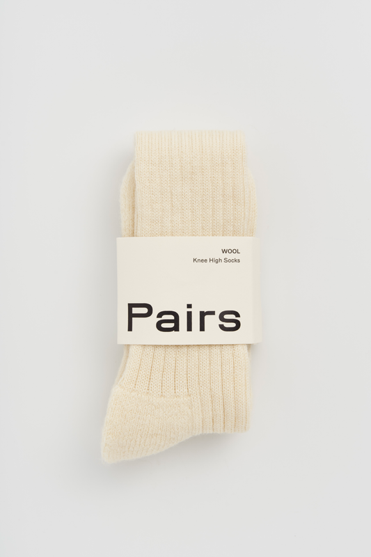 Pair of cream wool knee high socks with a 'Pairs' packaging band on a light grey background