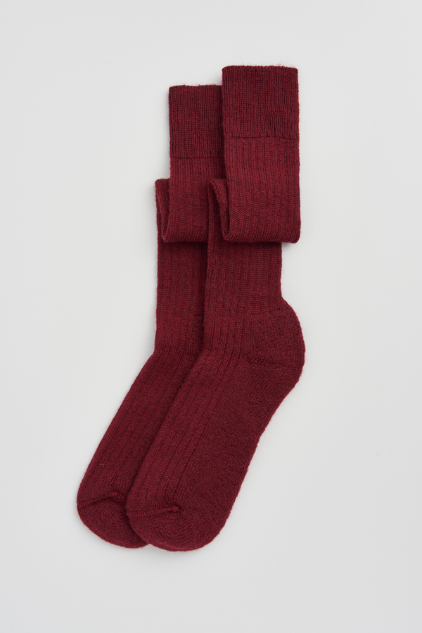 Pair of burgundy wool knee high socks on a light grey background