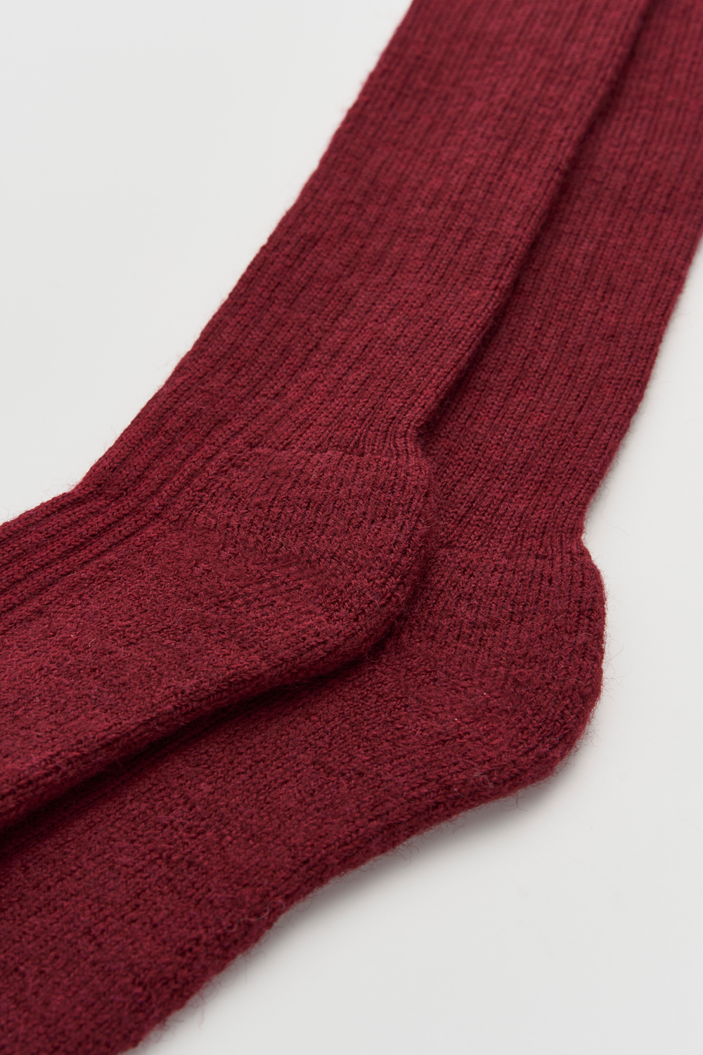 Close-up of the heel of a pair of burgundy wool knee high socks on a light grey background