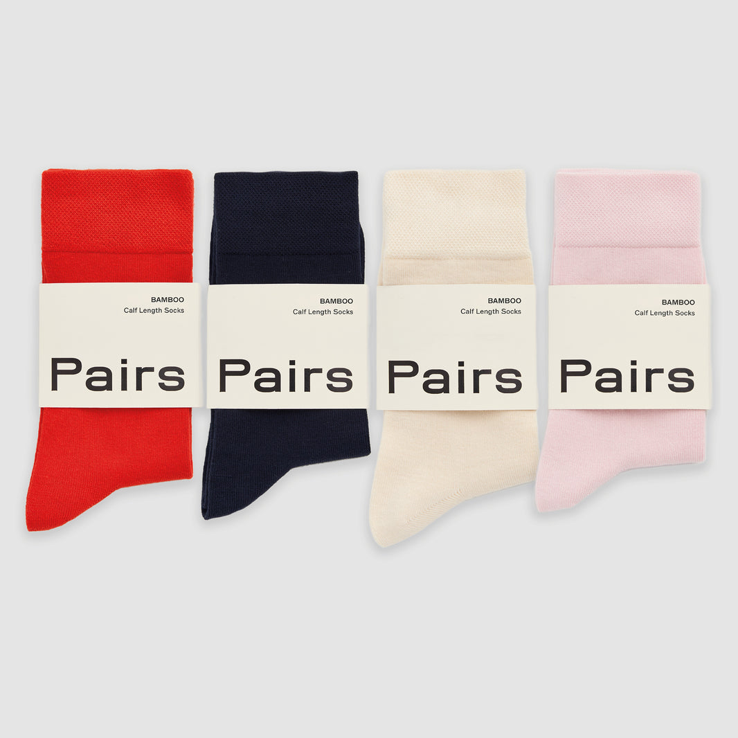Four bamboo socks in red, navy, cream and white, in 'Pairs' packaging on a white background.