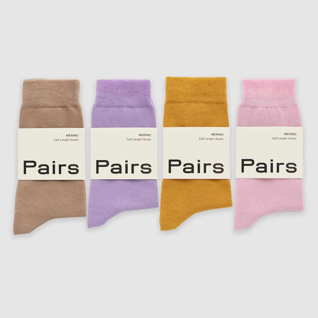 Four merino socks in beige, lilac, yellow and pink in 'Pairs' packaging on a white background
