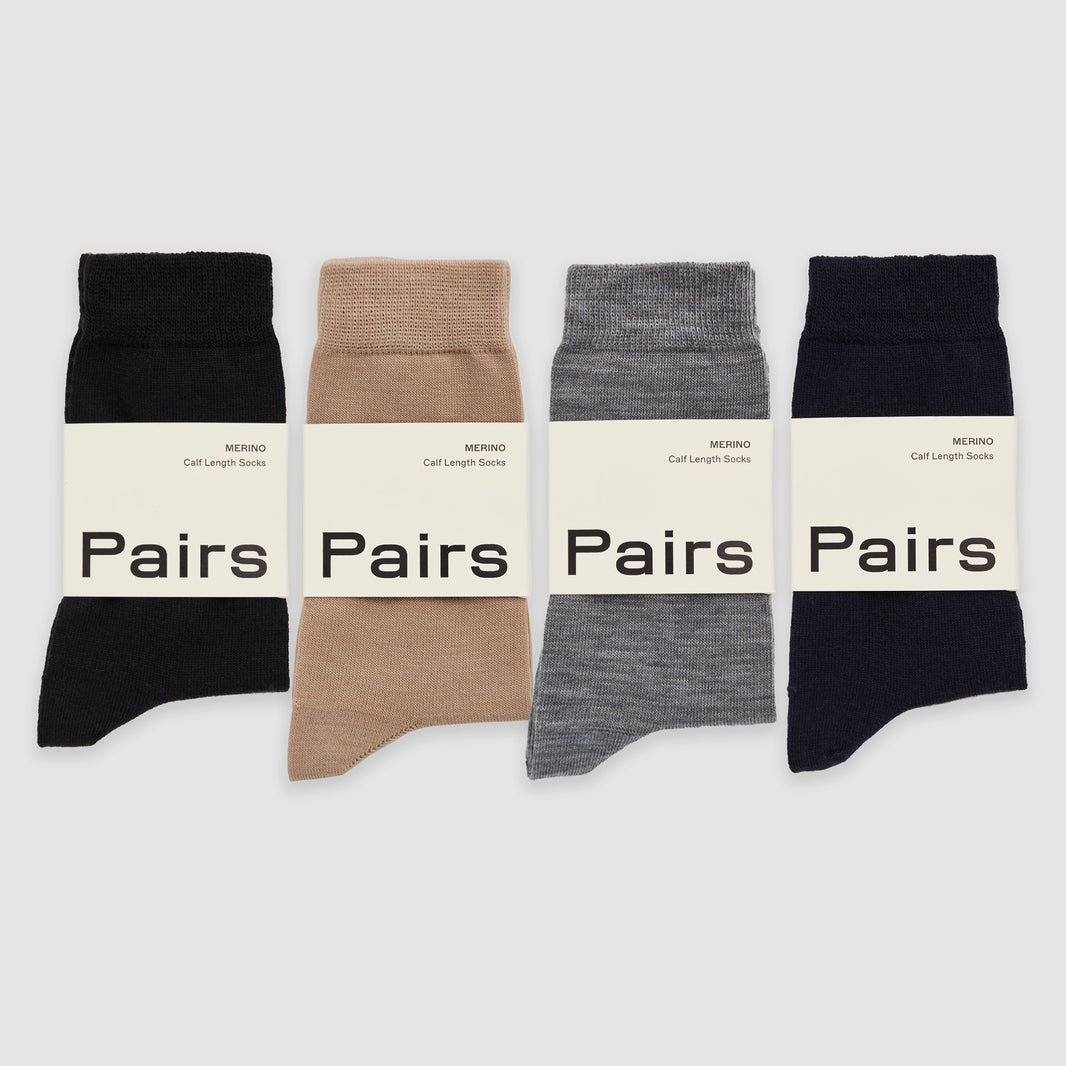 Four merino socks in black, beige, grey and navy, in 'Pairs' packaging on a white background