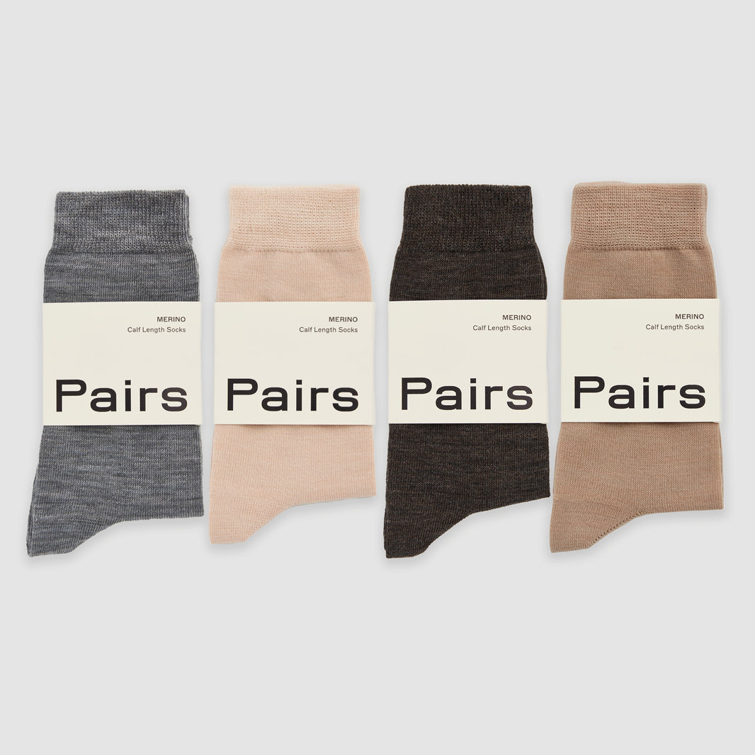 Four merino socks in grey, beige, and brown in 'Pairs' packaging on a white background.