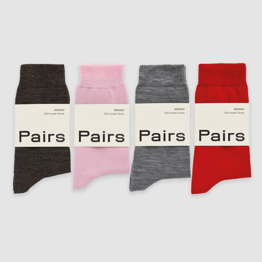 Four merino socks in brown, pink, grey and red, in 'Pairs' packaging on a white background